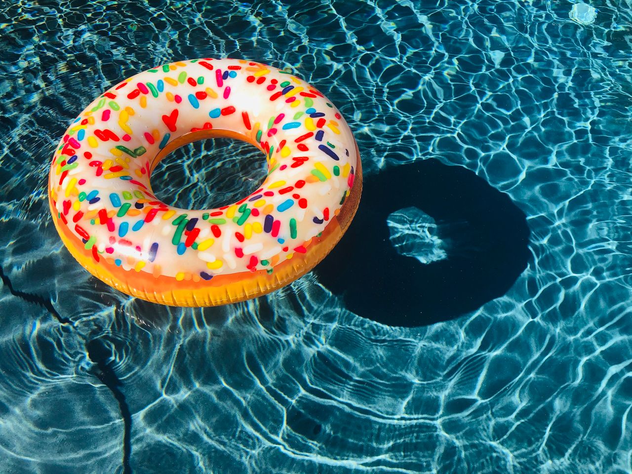 A vibrant donut-shaped pool float with sprinkles floating in a sunny swimming pool.